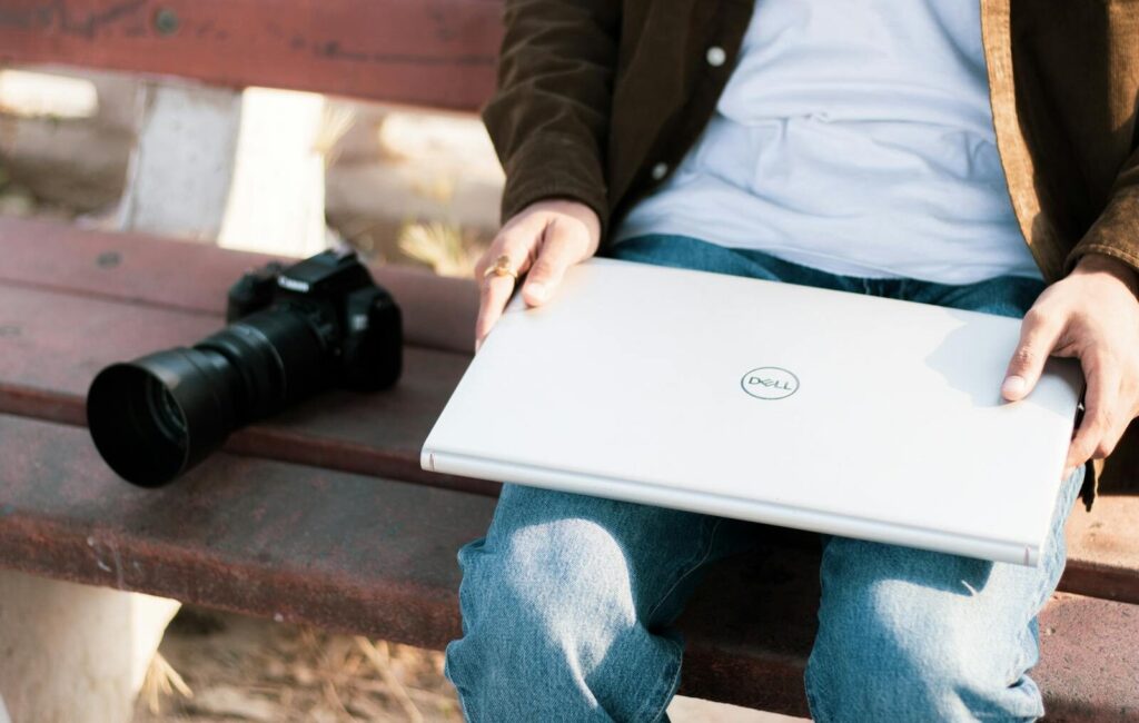 Kamera ve Laptop ile bir bankta oturan insan