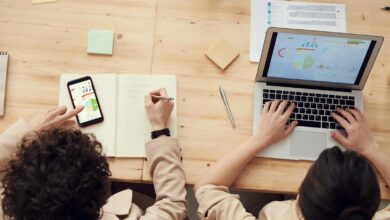 Overhead shot of two colleagues collaborating with devices and notes in a business meeting.