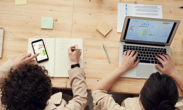 Overhead shot of two colleagues collaborating with devices and notes in a business meeting.